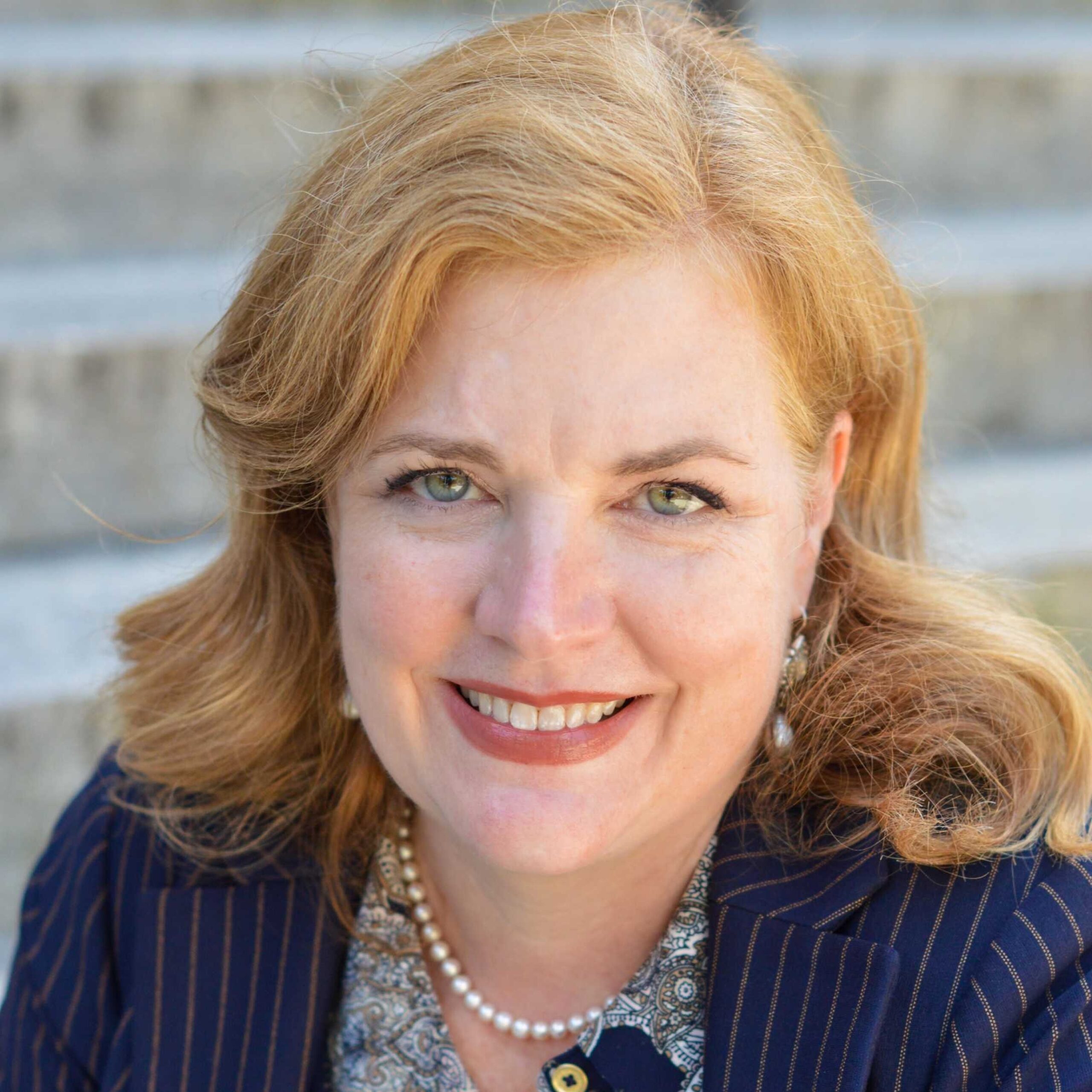 smiling woman with long strawberry blond hair in dark jacket against a brick background