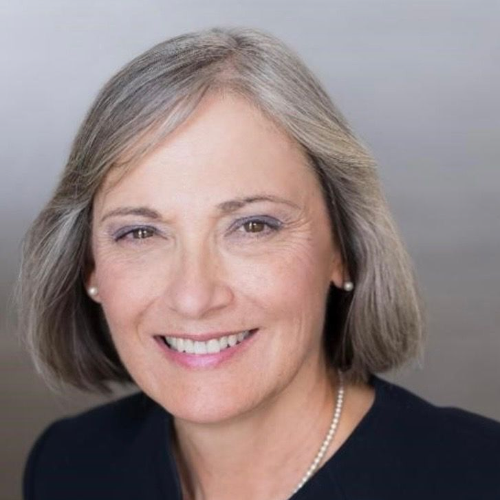 woman with short, light hair in a bob, wearing black top and pearls, smiling at the camera
